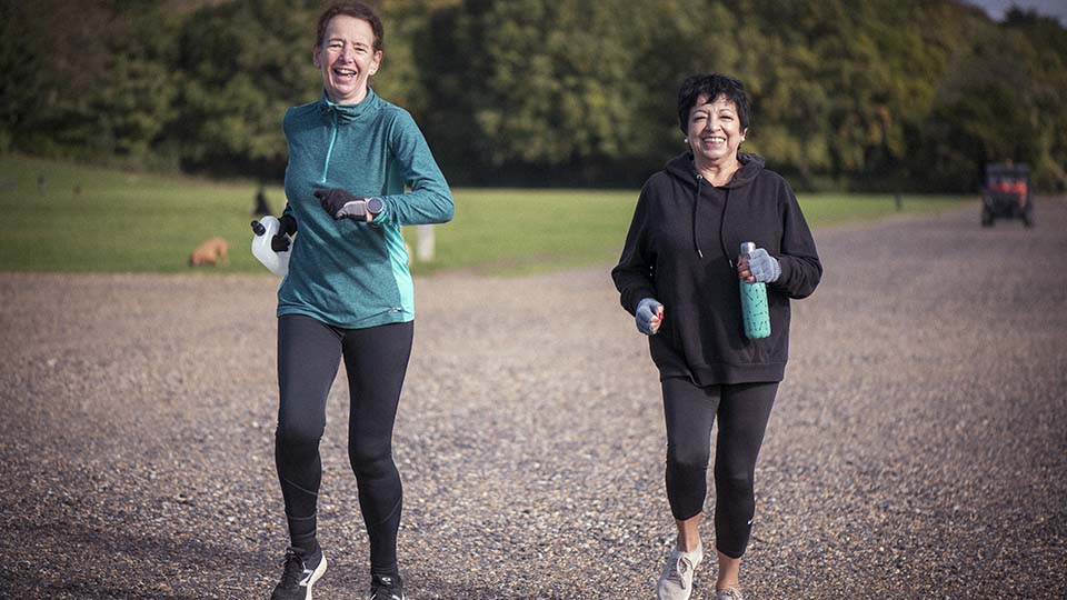 Two women jog outdoors on a gravel path